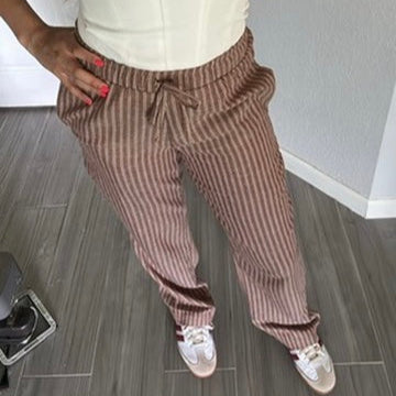 Person wearing a white tank top and brown striped pants in a room.